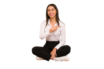 Young colombian woman sitting on the floor isolated smiling and pointing aside, showing something at blank space.
