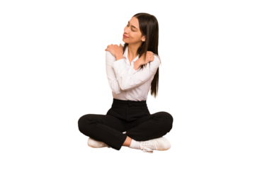 Young colombian woman sitting on the floor isolated hugs, smiling carefree and happy.