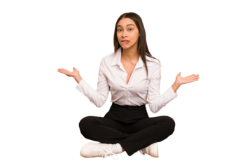 Young colombian woman sitting on the floor isolated confused and doubtful shrugging shoulders to hold a copy space.