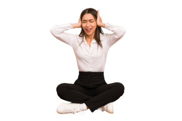 Young colombian woman sitting on the floor isolated covering ears with hands trying not to hear too loud sound.