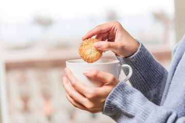Woman hands dipping cookie into coffee cup