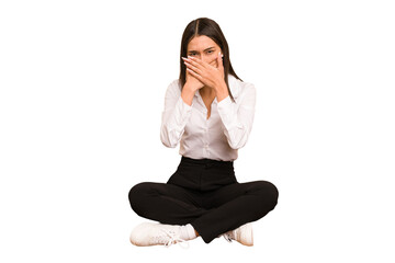 Young colombian woman sitting on the floor isolated covering mouth with hands looking worried.