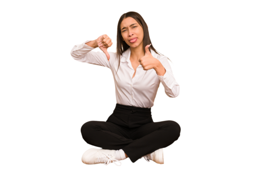 Young colombian woman sitting on the floor isolated showing thumbs up and thumbs down, difficult choose concept