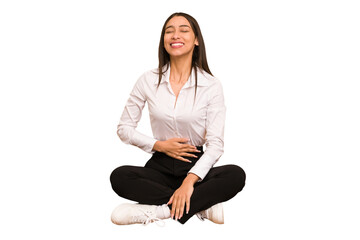 Young colombian woman sitting on the floor isolated touches tummy, smiles gently, eating and...