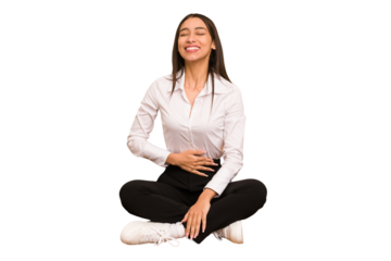 Young colombian woman sitting on the floor isolated touches tummy, smiles gently, eating and satisfaction concept.