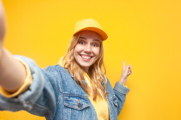 crazy girl in denim jacket and cap makes selfie on yellow isolated background