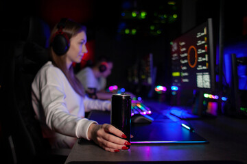 girl gamer sits at a computer and drinks an energy drink, a woman plays in a computer club at night...