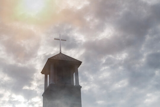 Sunshine breaks through a cloudy sky to light a cross on top of a church
