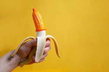 hand holds a banana with a condom, a contraceptive dressed on a sexualized banana on a yellow...