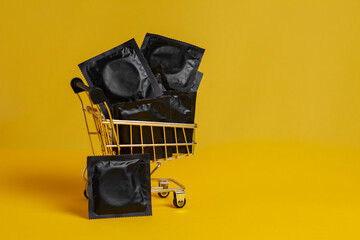 condoms lie in a shopping cart on a yellow background, buying contraceptives, discount concept
