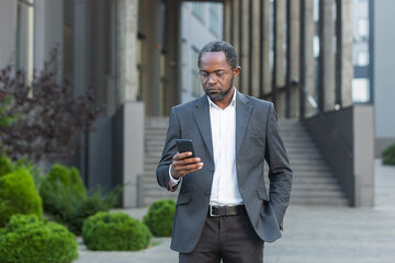 Serious and successful African American boss businessman outside office building using smartphone, man in business suit reading news online thinking and browsing internet pages. - Powered by Adobe
