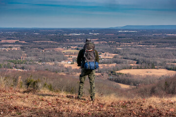 A man on a mountain looking from a cliff over the valley with a backpack filled with camping gear. At Keith Springs Mountain in Franklin County Tennessee USA.