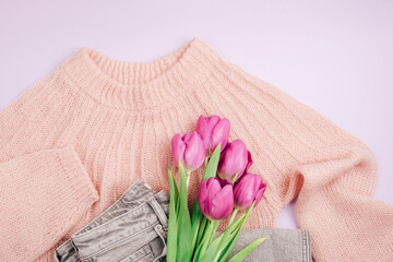 Bouquet of purple tulips on pink sweater and gray jeans. Casual clothes. Spring holidays concept. Top view, flat lay