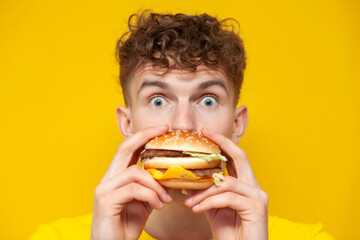 shocked guy eats a big burger and is surprised on a yellow background, a man bites fast food, close-up