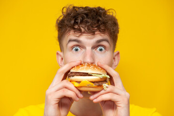 shocked guy eats a big burger and is surprised on a yellow background, a man bites fast food,...