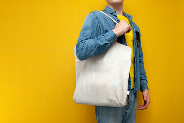Empty white silk fabric tote bag with handle. Close-up of a guy holding an eco or reusable shopping...