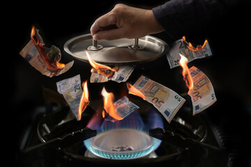 Gas price cap concept (German Gaspreisdeckel), stove with flames, burning euro banknotes flying upwards, hand holding a pot lid over it to limit the price growth during energy crisis, dark background - obrazy, fototapety, plakaty