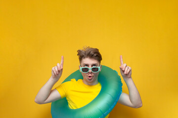 young guy with a swimming inflatable ring shows his hands up on a yellow background