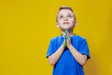 Ukrainian boy prays for Ukraine. Children against war. A boy in a blue T-shirt on a yellow...