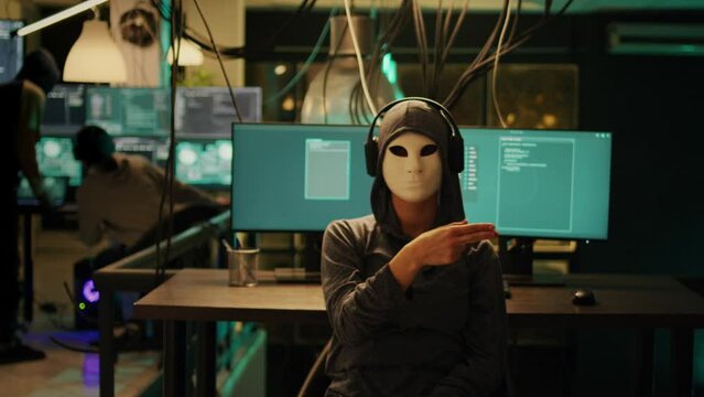Anonymous hacker with mask using hologram to hack computer server and steal information. Masked spy working with holographic data for cryptojacking and espionage, augmented reality.