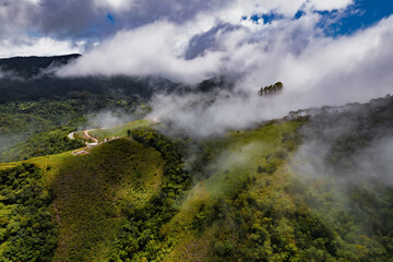 Aerial image of mountains with low clouds covering part of the landscape. Heavy clouds, green vegetation and very blue sky. Mist and white clouds.