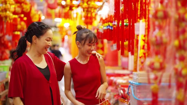 Happy Asian woman mother and daughter holding shopping bag during buy home decoration and joss paper for celebrating Chinese Lunar New Year festival at Chinatown street market. Chinese culture concept