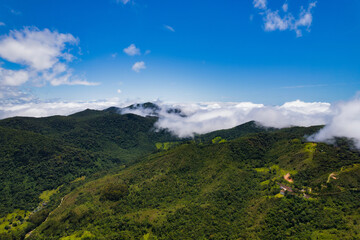 Naklejka premium Aerial image of mountains with low clouds covering part of the landscape. Heavy clouds, green vegetation and very blue sky. Mist and white clouds.
