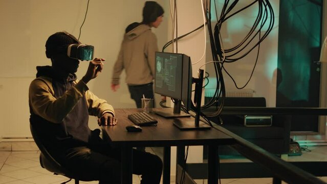 African american person hacking computer system with vr glasses, using virtual reality to steal passwords and data illegally. Young man using hacktivism skills to break into security server.