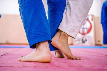 Legs of two young jiu-jitsu trainees in barefoot combat on a tatami floor.