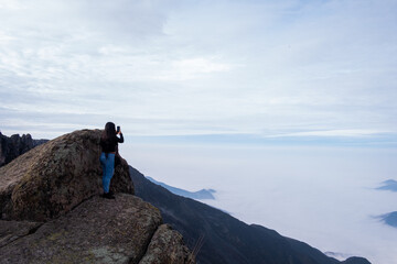 landscape where a latin woman sees a cushion of clouds, standing on the edge of a cliff in the Peruvian Andes.