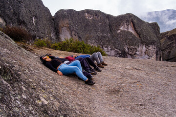 group of friends lying on a rock, on a plateau in the Peruvian Andes, where there are rocks and fog in the background.