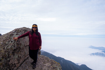latina woman smiling, standing on the edge of a cliff with a cloud bed in the background