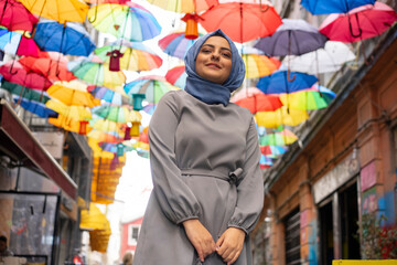 Girl in hijab, colorful umbrellas, sitting on chair. Young hijab girl poses for social media,