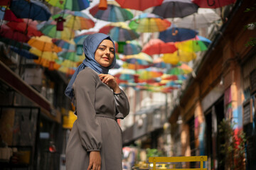 Girl in hijab, colorful umbrellas, sitting on chair. Young hijab girl poses for social media,