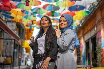 two woman hugging - with hijab and without. Colorful umbrella