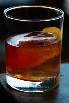 Old Fashioned Cocktail sitting on outside patio table with clear ice cube and orange peel garnish - Closeup