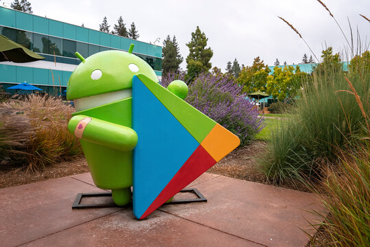 San Francisco, USA. September 20, 2022. Statue of Android with play store logo amidst plants and grass in garden outside office building at Google campus during sunset