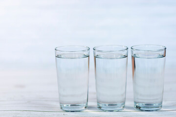 Three water glass on wood white ground and there is a light shining from behind the white background.