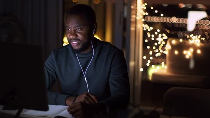 Young african american man student in earphones studying late in evening at home, watching personal lesson with tutor