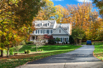 private two-storey house among autumn trees. Asphalt driveway to garage. - obrazy, fototapety, plakaty