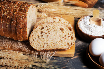 Wheat flour, sliced bread  with sesame seeds, wheat ears and straw on an old wooden background