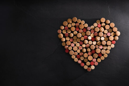 Heart made of wine bottle corks on black table, top view. Space for text