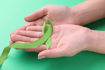 World Mental Health Day. Woman holding green ribbon on color background, closeup