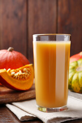 Tasty pumpkin juice in glass and different pumpkins on wooden table