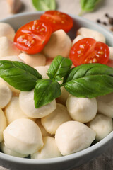 Delicious mozzarella balls, tomatoes and basil leaves in bowl on table, closeup