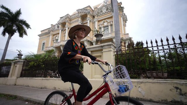 Laughing, happy, fun mature elderly woman in ethnic clothing and hat biking on the Central Avenue Paseo de Montejo with museums, restaurants, monuments and tourist attractions in Merida Yucatan Mexico