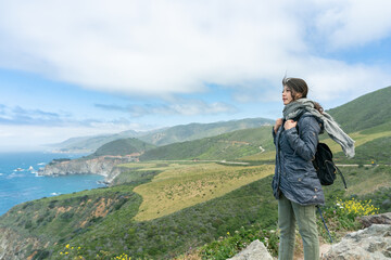 asian taiwanese woman backpacker overlooking scenic ocean and mountain view under blue sky while touring big sur in california usa