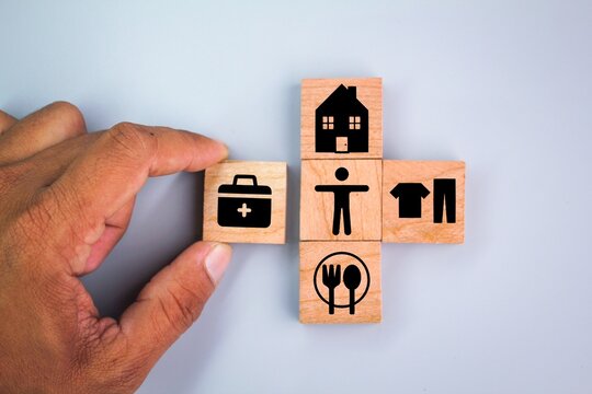 wooden cube with icons of food, Clothing, housing, medical bag, four basic human needs concepts. The Four Basic Material Needs of the Human Being.