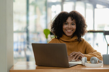 African american girl writing in notebook sitting at desk with laptop. Working hard. Woman wearing headphones while working online. Student excited to learn language online in cafe.