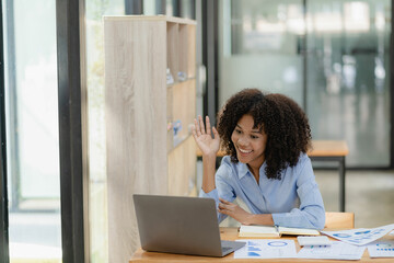 Young happy successful business woman working with laptop and calculating analytical calculator with financial graph document in office online meeting concept